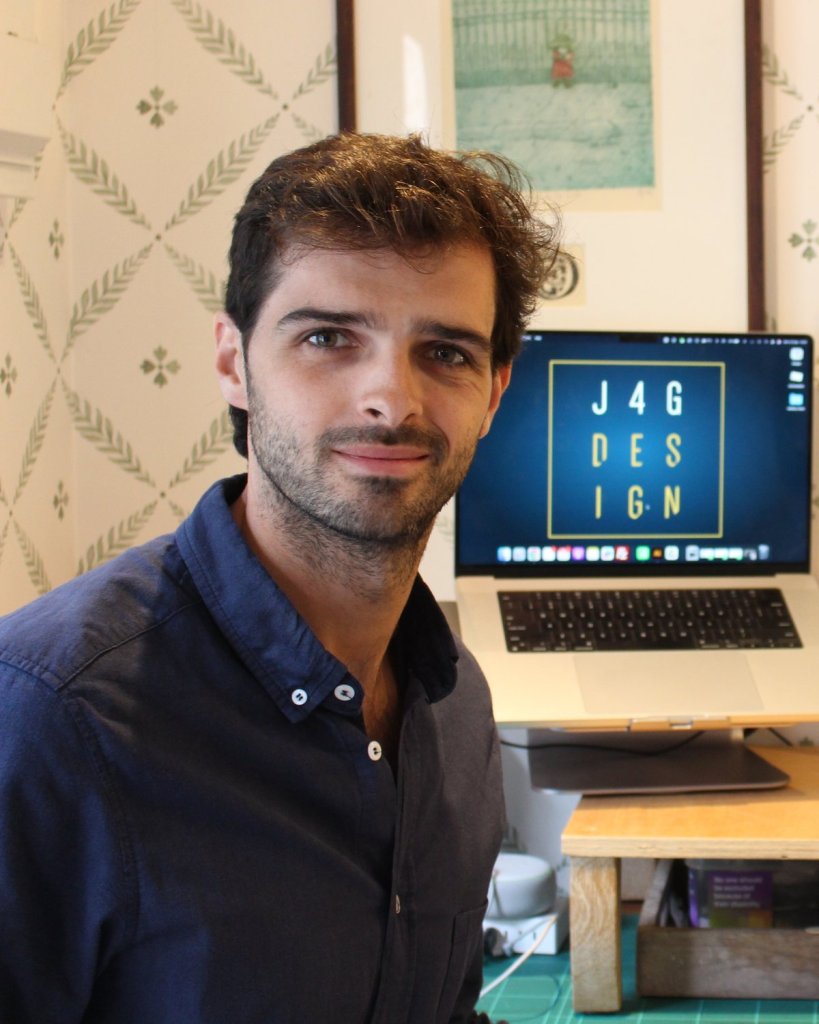 Christopher Mollard, founder of J4G Design, at his studio desk in Fulham with the J4G Design logo on screen